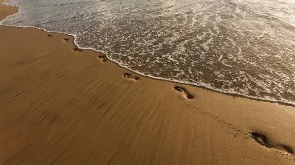 Pegadas na areia perto do mar ao pôr do sol — Fotografia de Stock