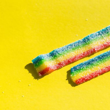 Sarı arka plandaki şekerde çizgili, renkli marmelat. Gökkuşağı renkli marmelat şekeri. Boşluğu kopyala, metin için boş şablon