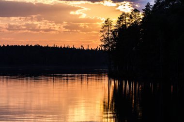 Gölde fantastik bir gün batımı, sakin sularda yansıyan karanlık çam ormanı.