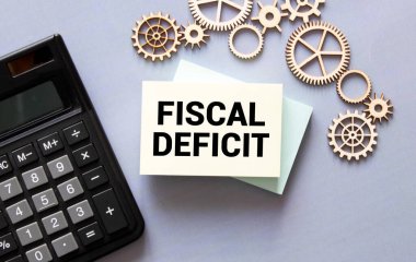 FISCAL DEFICIT kelimeleri arka planda tahta küplerin, banknotların, siyah hesap makinelerinin ve yeşil bitkilerin yanında beyaz kağıt üzerinde yazılmıştır. İş, Mali ve Eğitim kavramı.