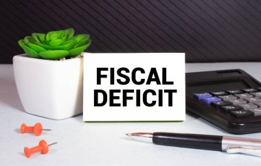 Beyaz arkaplanda notlar, hesap makinesi ve kum saati için FISCAL DEFICIT kağıdı içeren beyaz kart.
