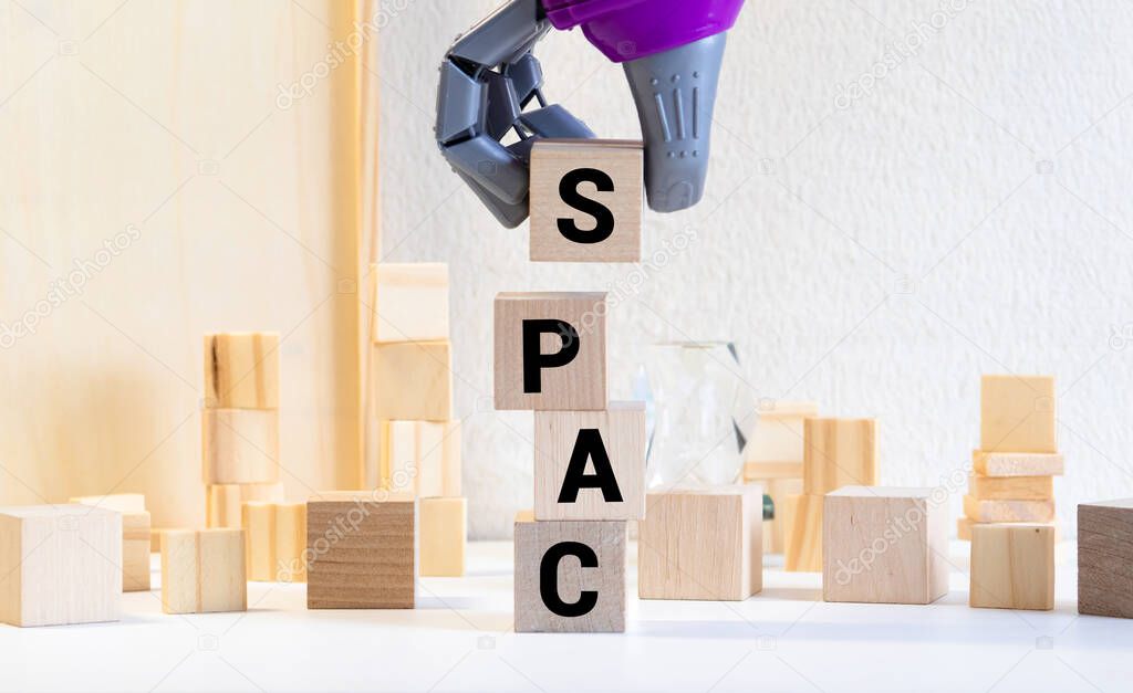 SPACs symbol. Wooden cubes with words 'SPACs, special purpose acquisition companies' on beautiful black background, copy space. Businessman hand. Business and SPACs concept.