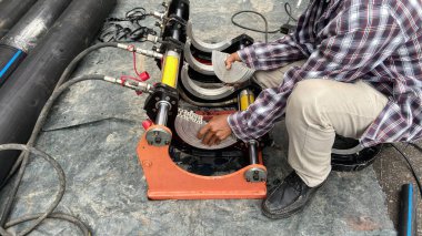 Tesisatçı, fabrikadaki boruları bağlamak için hidrolik bir PE kaynak makinesiyle tesisat üzerinde çalışıyor..