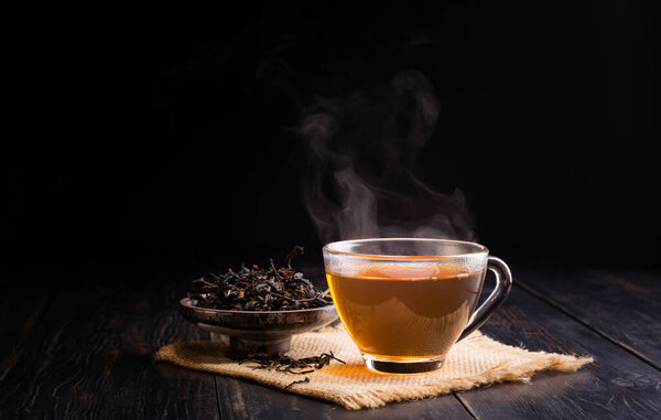 hot herbal teacup and dried tea leaves in a ceramic cup placed on a black wooden table on, dark background
