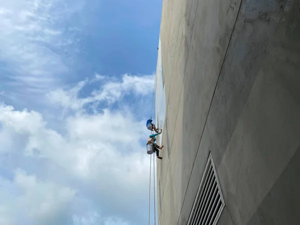 建物の壁に壁や絵を描く画家高さの高い建物に安全装置のないローラーブラシで作業する建設労働者高さで危険な仕事の概念 — ストック写真