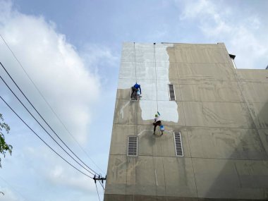 Duvarı tamir eden ve inşaat işçisinin duvarını boyayan boyacı. Paten fırçasıyla yüksek binalarda güvenlik ekipmanı olmadan çalışıyor. Yükseklerde tehlikeli iş kavramı.