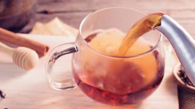 Çayı yavaş çekimde buharlı bir çay fincanına boşalt. Koyu siyah arkaplan ve açık güneş ışığı. Sıcak bir atmosferde parlıyor.