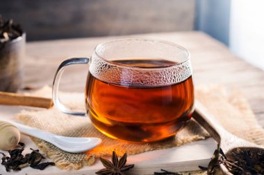 hot tea in a teacup A glass of tea is placed on an old wooden table. on black background, light sunlight shines in a warm atmosphere