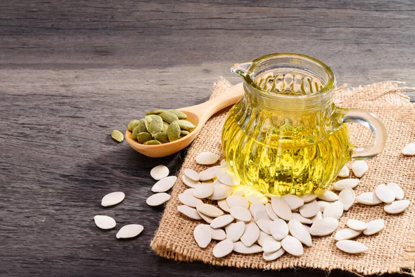 Pumpkin seed oil in a pitcher with pumpkin seeds placed on an old wooden table.