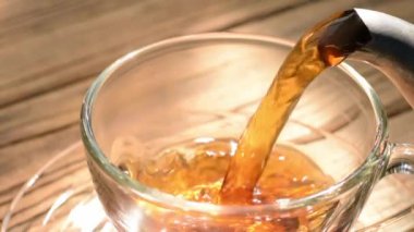 Yavaş çekim videosu, basit bir ahşap masaya yerleştirilmiş şifalı otlarla beyaz bir çay fincanına dökülen sıcak çayı gösteriyor..