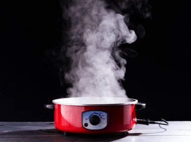 Elektrikli tencere ya da haşlama çorbası. Mutfakta yemek pişiren ve kaynar su içen insanlar için siyah zeminde duman var..