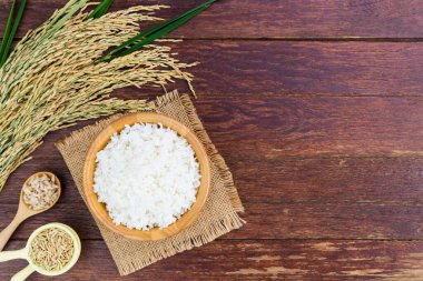 White rice or jasmine rice in a wooden bowl with yellow ears of rice placed on a wooden floor or a needle-colored table - top view