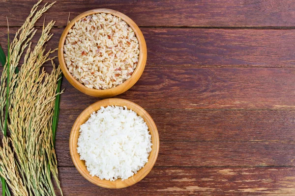 White rice or jasmine rice and brown rice in a wooden bowl with yellow ears of rice placed on a wooden floor or a needle-colored table - top view