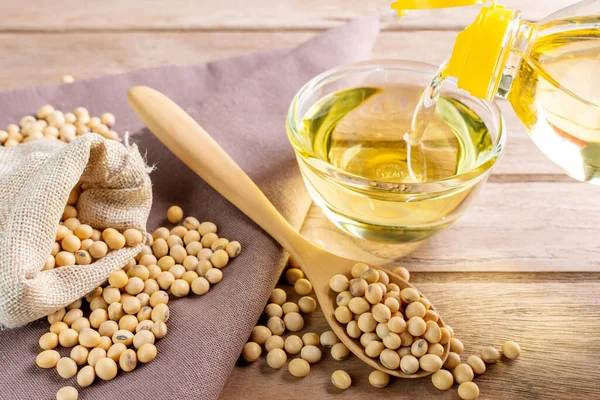 Pour the soybean oil into a glass cup. and put soybeans on a wooden table Natural healthy food - top view
