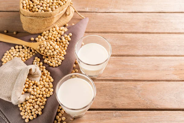 Soy milk in a glass with soybeans on a wooden table organic drink high protein healthy breakfast agricultural produce vegetarian - top view