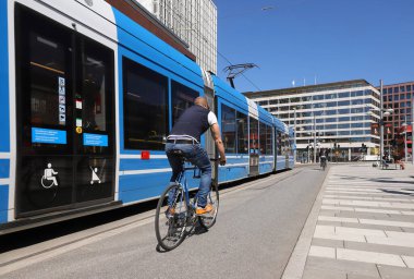 Stockholm, İsveç - 12 Mayıs 2021: Sergels Torg Meydanı 'nda modern bir tramvayın yanında bir adam bisiklet sürüyor.
