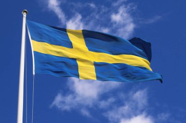Düşük açılı, hafif bulutlu mavi gökyüzüne karşı dalgalanan İsveç ulusal bayrağının görüntüsü...