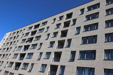 Açık mavi gökyüzüne karşı inşa edilen modern çok katlı bir apartmanın alçak açılı görüntüsü.