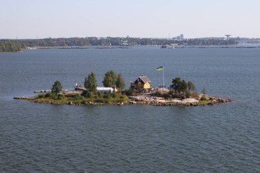 Helsinki, Finland - August 20, 2022: The Ukrainian flag raised next to a small house on a small island arriving ship in the Helsinki harbor entrance.
