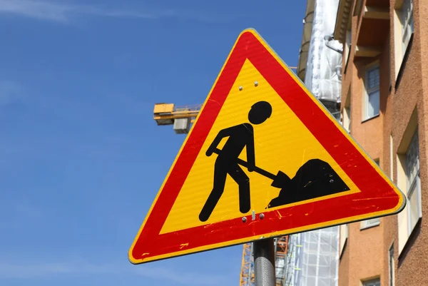 Genderless road work warning sign in front of a construction site.