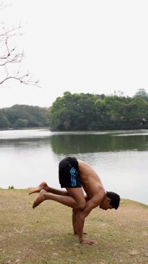 Brezilya 'lı genç adam, gölün kenarında bulutlu bir günde yoga yapıyor, uçan güvercin..