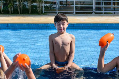 Çocuk havuzun kenarında oturuyor ve birkaç su bombası tarafından vurulmaya hazır..