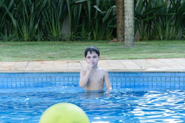 8 yaşında bir çocuk havuzda endişeli görünüyor ve tırnaklarını kemiriyor. Top atışını bekliyor..