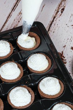 Seçici odaklanma. Çikolatalı tartlara krem şanti sürerken şekerlemecinin başlığını kapatıyoruz..