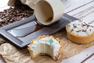 Tereyağlı küçük turta ve bir ısırıkla birlikte beyaz çikolatalı ganache, ters dönmüş bir fincan kahvenin yanında..