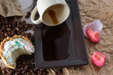 Bir ısırıklı mini beyaz çikolatalı ganache turtası, devrilmiş bir fincan kahve tugayının yanında..