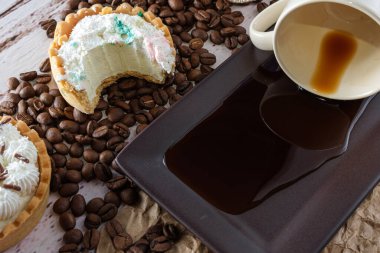 Tereyağlı mini turta ve bir ısırıklı beyaz çikolatalı ganache, ters dönmüş bir fincan kahvenin yanında..