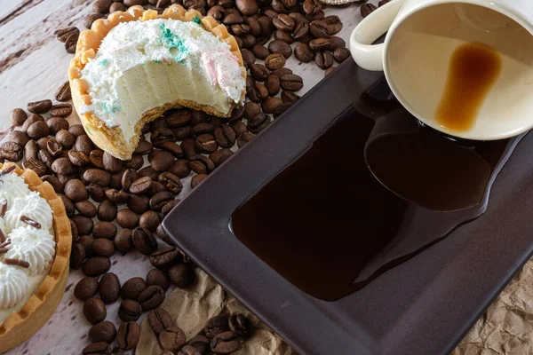 Tereyağlı mini turta ve bir ısırıklı beyaz çikolatalı ganache, ters dönmüş bir fincan kahvenin yanında..