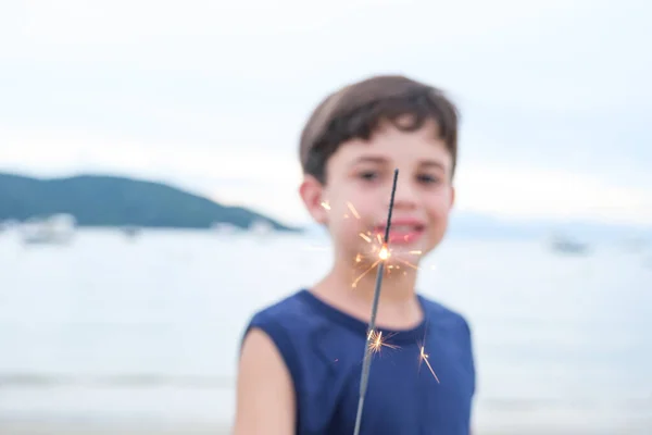 A candle sparkles focused in the foreground. In the blurred background, an 8 year old child.