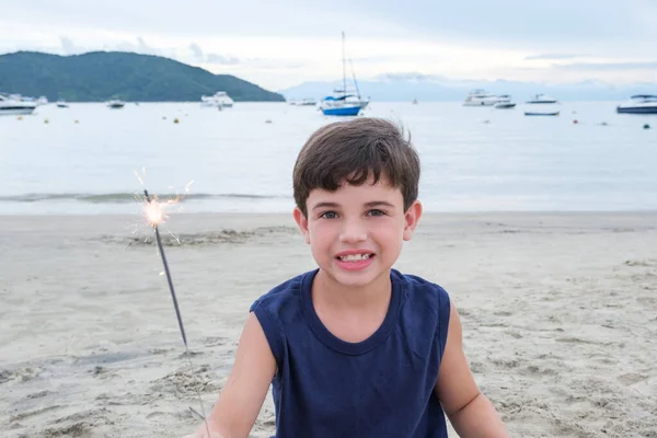 Smiling Brazilian child of 8 years old holding a candle sparkles on the beach sand.