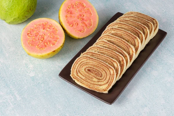 Sliced roll cake on a brown plate next to guavas.