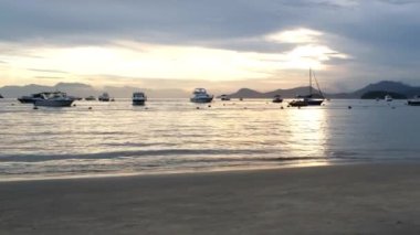 Gün batımında tekneler ve yatlar aydınlatılıyor, küçük bir tekne hızla geçiyor..