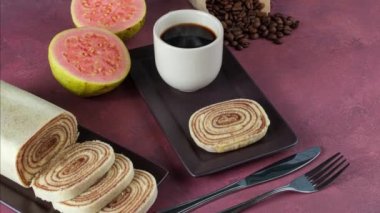 Kırmızı arka planda guava, kahve ve kahve çekirdekleri ile çevrili bir dilim bolo de rolo..