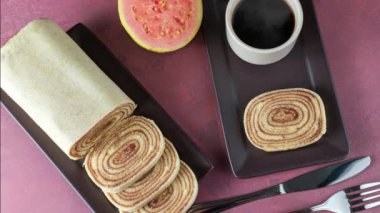 Kırmızı zemin üzerinde guava, fincan ve kahve çekirdekleri ile çevrili bir bolo de rolo dilimi (üst görünüm).