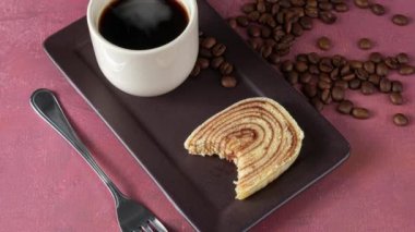 Bolo de rolo dilimi, çatal, fincan ve kahve çekirdeğinin yanında..