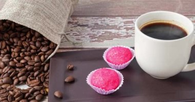 Brigadeiros bichos de pe yanında bir fincan ve kahve çekirdekleri (kenar görünüm).