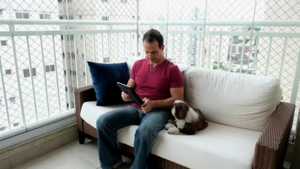 男人坐在白色的沙发上抱着他的宠物 旁边有一个视频通话 — 图库视频影像