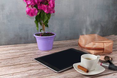 Tablet kahve fincanı, ruj ve makyaj çantası ile çevrili..