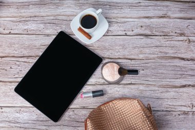 Kahve fincanı, ruj ve makyaj çantası ile çevrili tablet masanın üzerinde..