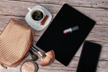 Kahve fincanı, makyaj çantası, akıllı telefon, pres tozu ve fırçalarla çevrili ruj tableti..