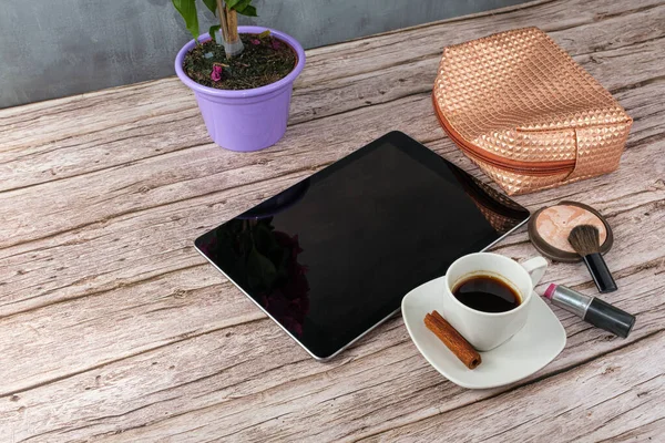Tablet kahve fincanı, ruj ve makyaj çantasıyla çevrili..