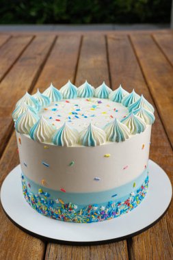 Vanilyalı kekin üstüne tereyağlı krema süslemeli yakın plan. Arka plandaki bahçe _ dikey.