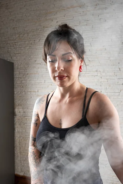 Brazilian tattooed looking at the smoke coming out of the pot.
