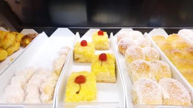 Soft cake topped with sugar syrup, cherry and grated coconut. In a bakery showcase.