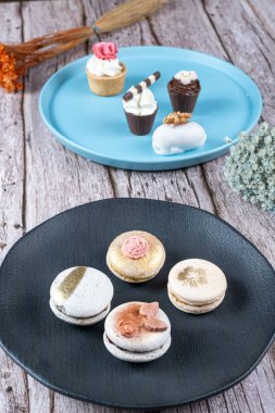 Macarons decorated with edible ink and fondant. In the background assorted sweets with whipped cream and nuts.