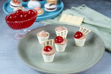 Closeup of small white chocolate cups filled with milk chocolate mousse. Next to cherries and wedding candies.